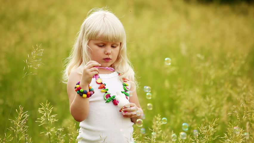 Child blowing bubbles. She laughs and look at camera. 