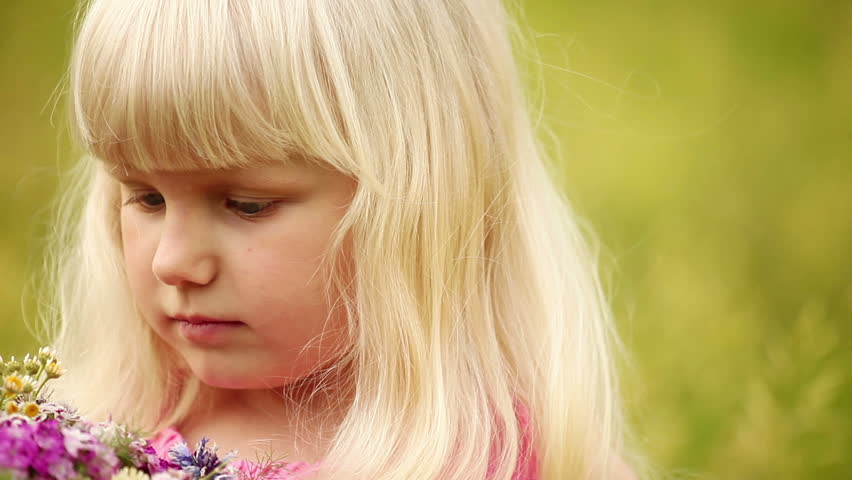 Close up portrait of a little blonde with flowers. Looks at camera