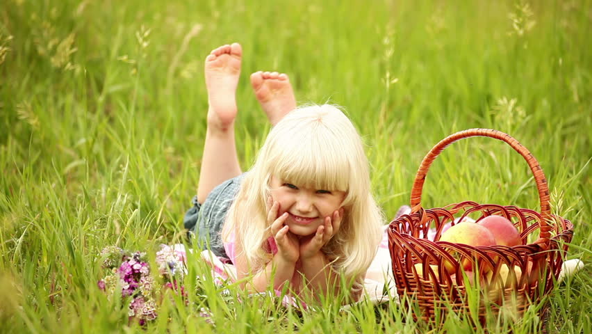 Little blonde child lying on the grass. Next basket of apples 