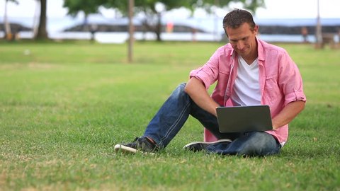 Smiling Man With Laptop Talking On Mobile Phone In The Park