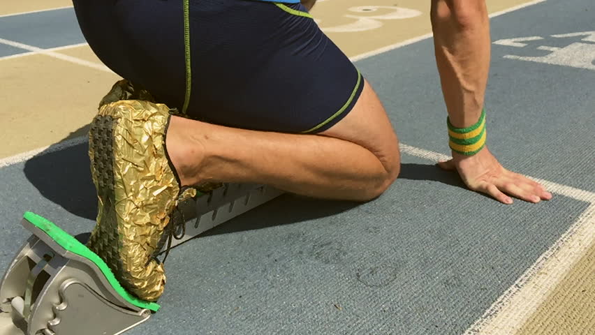 Athlete in gold shoes starting a race in slow motion from the starting blocks on a blue running track 