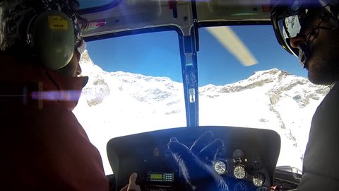 Two men in helicopter cabin flying in snow mountains