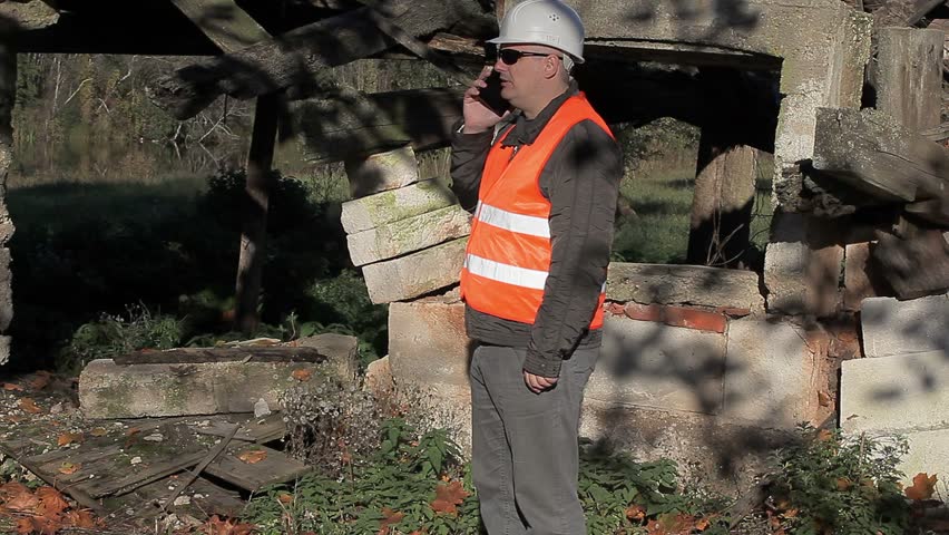 Building inspector talking on smartphone near destroyed building