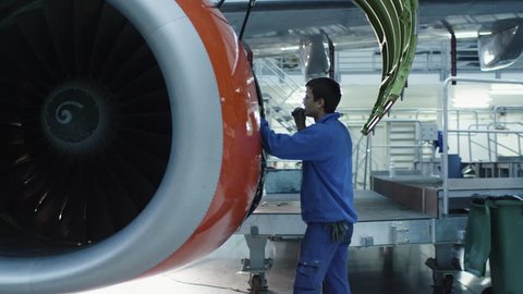 Aircraft maintenance mechanic with a flash light inspects plane engine in a hangar. Shot on RED Cinema Camera in 4K (UHD).