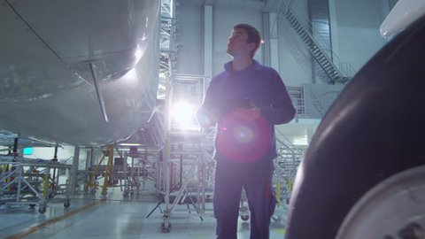 Aircraft maintenance mechanic uses tablet to inspect plane body in a hangar. Shot on RED Cinema Camera in 4K (UHD).
