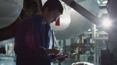 Aircraft maintenance mechanic uses tablet to inspect plane chassis in a hangar. Shot on RED Cinema Camera in 4K (UHD).