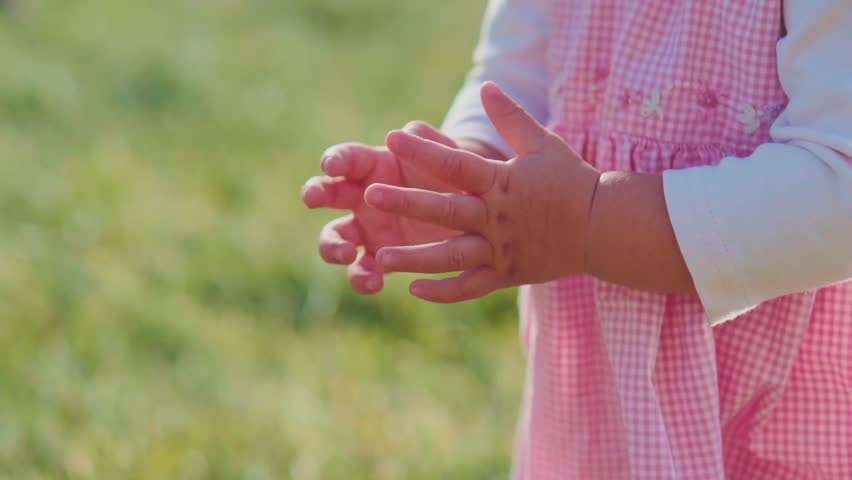 Cute baby girl is clapping hands and having fun outdoors in summer. Slow motion filmed at 240 fps. Toddler hands close up. Close up on hands. Happy childhood concept. 