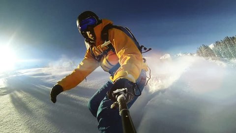 Man riding on snowboard with selfie stick in his hand