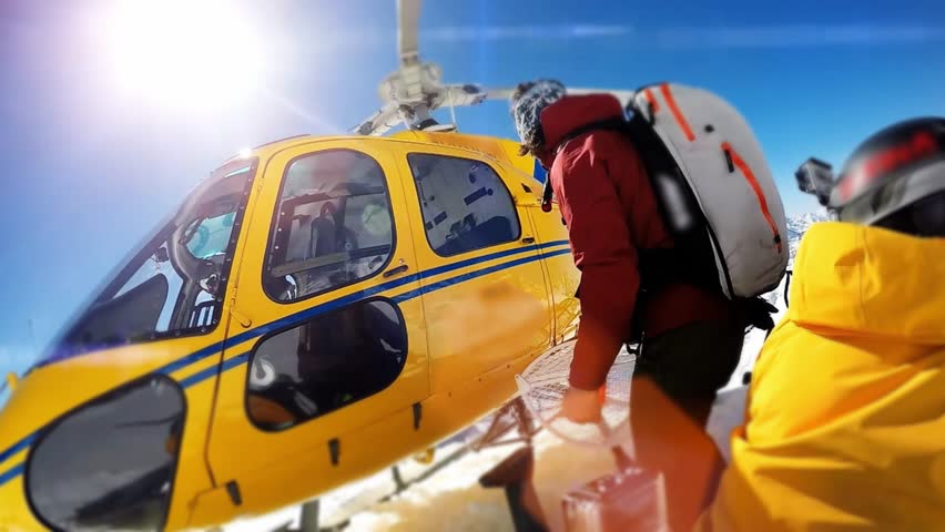 Actionsportlers were dropped by a helicopter at the top of the mountains. The sun is shining brightly in the blue sky. There is a mountain range in the background covered in snow. Royalty-Free Stock Footage #12186776