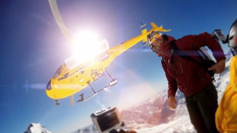 Actionsportlers were dropped by a helicopter at the top of the mountains. The sun is shining brightly in the blue sky. There is a mountain range in the background covered in snow.