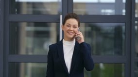 Slow motion video of confident businesswoman using smart phone. Beautiful professional outside work place. She is walking outside office building.