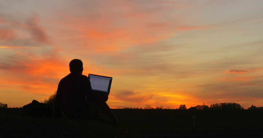 Man With Laptop is Sitting Man's Silhouette at the Sunset Freelance Programmer, Designer, Freelance Copywriter, Accountant, Man's Back, Man Stands Up ,People are walking by, people silhouettes, Royalty-Free Stock Footage #12188270