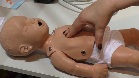 Woman's hand performing cardiac heart massage or CPR on a child mannequin