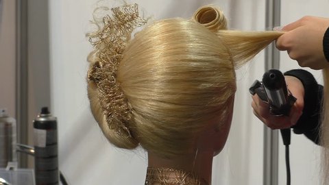 Hair designer or stylist is making curls on a female mannequin blond hair at hairdresser salon