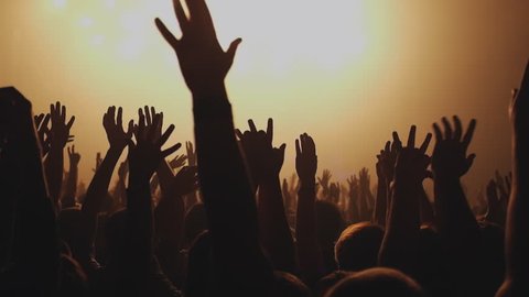 Lot of people clapping at rave party. Here is  footage of people crowd partying at a concert or a night club. You can see dark silhouettes dancing, jumping and waving hands in front of stage.  
