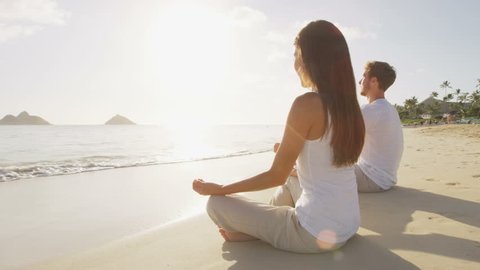 Meditation. Yoga people by the sea relaxing in serene zen lotus yoga pose on a beach at sunrise. Woman and man meditating together.