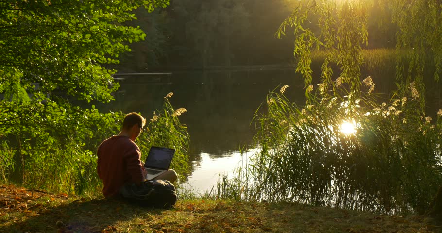Man in Glasses is Working with Laptop, Sitting at The Lake With His Face to the Sun, Freelancer Programmer Copywriter Designer Accountant, Put the Laptop Away, looking at the water, Forest Lake, Royalty-Free Stock Footage #12195878