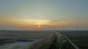 Flight over an open cast mine at sunset with a wind power energy farm in background
