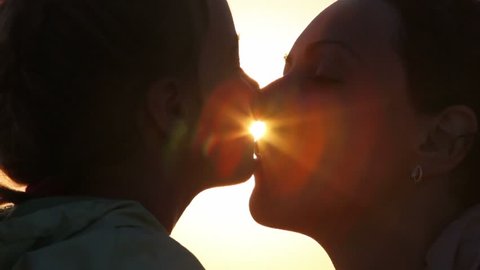 Silhouettes of mother and her daughter heads, daughter kisses mother