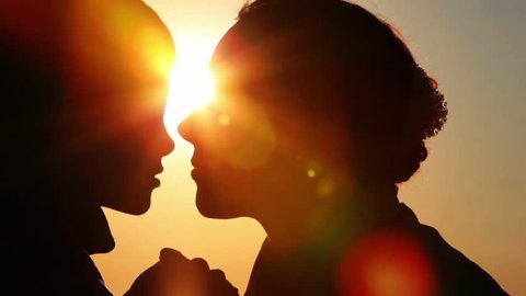 Silhouettes of mother and her son heads,  nose to nose and holding hands, mom tell something to son