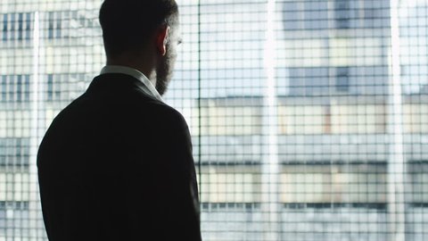 Businessman in a suit stands next to a big window and uses smartwatch on a sunny day. Shot on RED Cinema Camera in 4K (UHD).