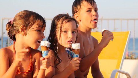 three kids eat ice cream in waffle cone, little girl shows off somewhere arm summer by sea