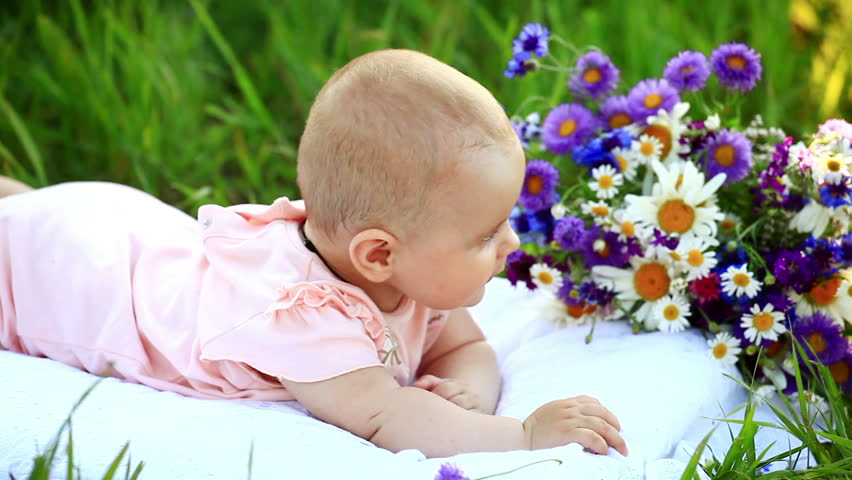 Baby in the grass with flowers. His turned at camera. 