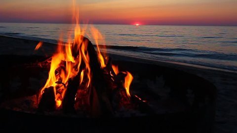 Campfire burns brightly at sunset along the beautiful beach of Lake Superior in northern Michigan