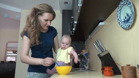 Careless mother woman feed baby on table in kitchen at home. Infant child eat food mash from spoon. Static shot. 4K UHD video clip.