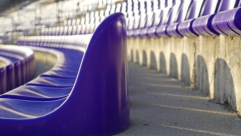 Rows of violet plastic seats on empty stadium tribune, dolly. COVID-19 quarantine.
