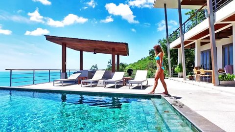 Beautiful woman walking around pool. Nice sea view from luxury villa. Legs.