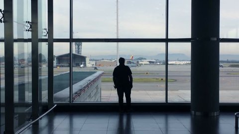 Silhouette of a person looking out at the window of the terminal. Waiting to embark inside airplane. Man lost in contemplation looking at planes pass by. Blue tone