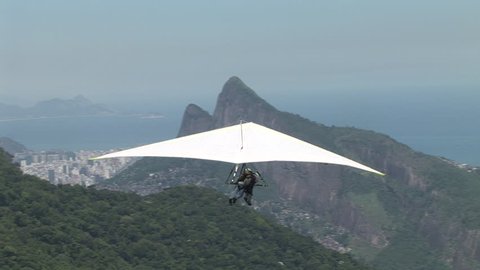 Fantastic Close Up shot of hang glider taking off from atop a mountain. Static Camera at first then Zoom in to track the flight. Shot in Rio de Janeiro, Brazil.