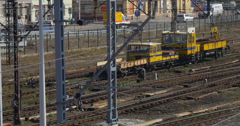 Worker in Orange Workwear on Railroad, Yellow Locomotive is Moving Slowly by Railroad Moving, Cars at the Street, Railway Station in Opole Poland, railroad junction, Road behind the Station, Wire