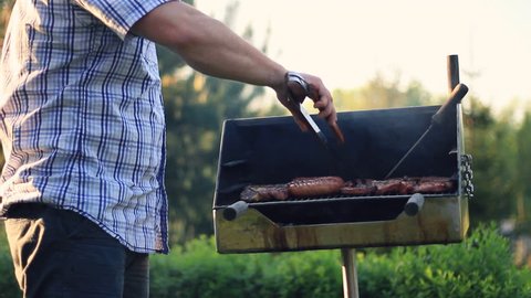 Man cooking meat on the barbecue grill and smiling to camera, outdoors, camera stabilizer shot