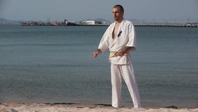 Karate Kimono Male Fighter Winner Victory slow-motion Stock Video Footage Man on the beach practicing, he does exercise. Behind him ships, seascape, sky, summer hdv Static, Hd, Hidef, Fx, Definition