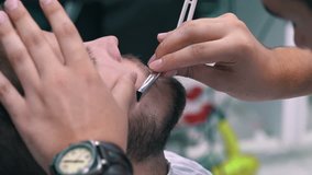 Barber cuts the beard of the client with blade at a barber shop