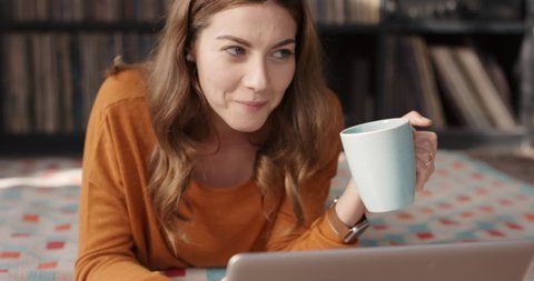 Cool happy woman laughing at funny streaming movie on laptop at home drinking coffee having fun alone