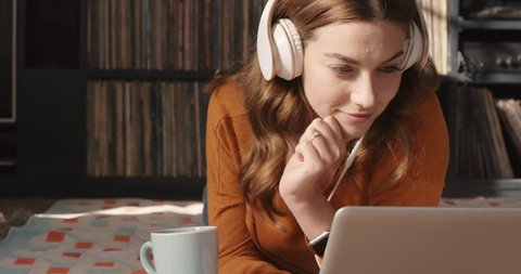 Beautiful woman listening to music on laptop at trendy home with headphones drinking coffee smiling vintage records in background orange retro colours and styling