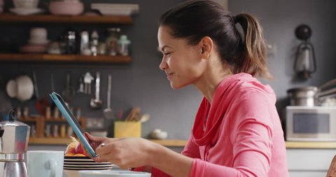 Beautiful Mixed race woman talking to friend eating breakfast at home using digital tablet app video messaging
