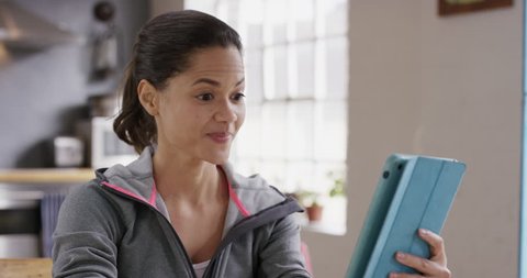 Happy mixed race woman having video chat talking to her friend online using digital tablet app at home wearing sportswear in kitchen