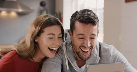 Attractive young couple at home laughing at funny internet joke online using digital tablet having fun