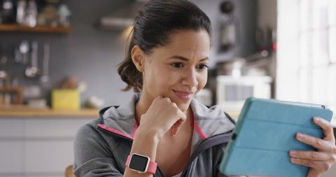 Happy mixed race woman laughing while watching funny internet video using digital tablet at home wearing sportswear