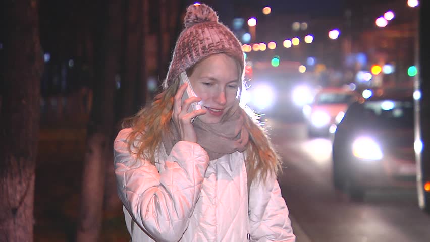 Girl talking on the phone in the evening on the street. Rejoice, smiling. Passing vehicles.