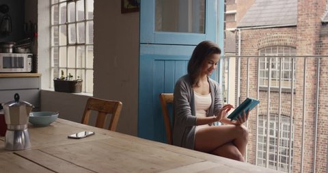 Beautiful Mixed race woman at home using digital tablet app happy loft apartment wearing pajamas talking to friends using internet
