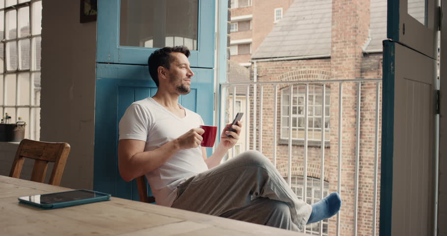 Handsome man at home drinking coffee using smartphone loft apartment in pajamas relaxing Royalty-Free Stock Footage #12270185