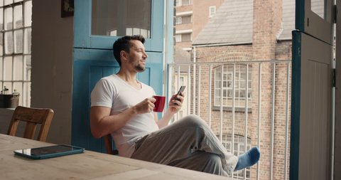 Handsome man at home drinking coffee using smartphone loft apartment in pajamas relaxing