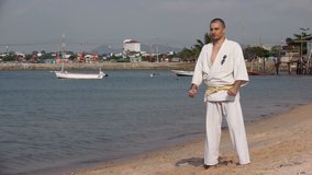 Motion Slow Karate Kimono Stock Video Footage Man on the beach practicing, he does exercise. Behind him ships, seascape, sky, summer hdv Static, Hd, Hidef, Fx, Definition, High