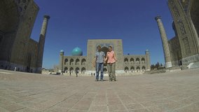 Couple of tourists holding hands and jumping on the middle of Registan Square in Samarkand, Uzbekistan.