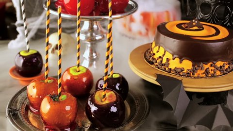 Table with colored candy apples and cake for Halloween party.
